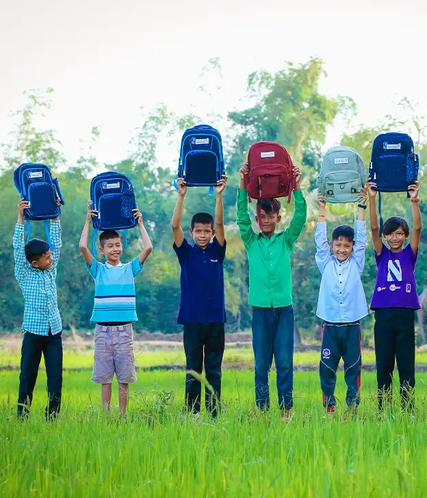 A group of students smile and hold up their backpacks.