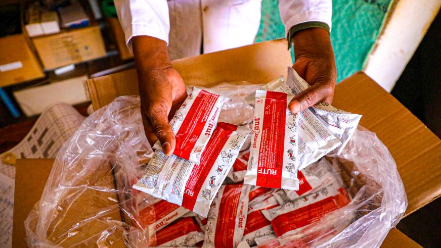 Hands hold several packets of ready-to-use therapeutic food (RUTF) taken from a box of individually packaged nutritional supplements. (Ethiopia, 2026)