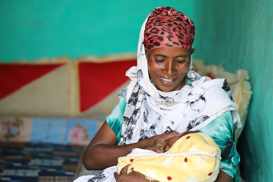 An Ethiopian woman comfortably breastfeeds her baby in her home.