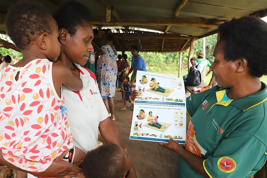 A healthcare worker holds an educational book to teach a mother about how to breastfeed.