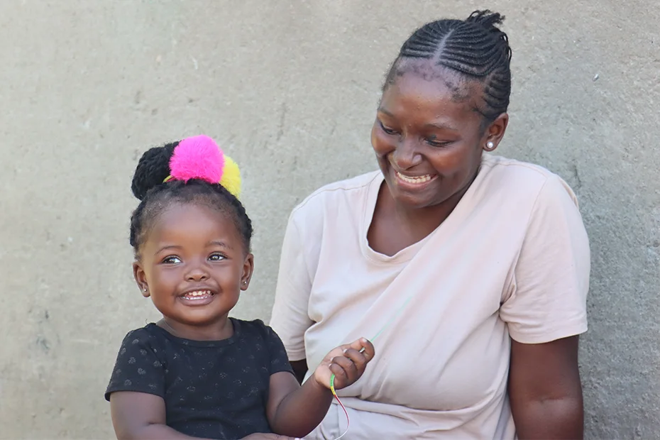 A woman and her toddler daughter smile and play together.