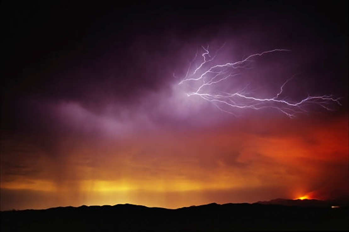 Lightning flashing over the sky while a fire burns below.