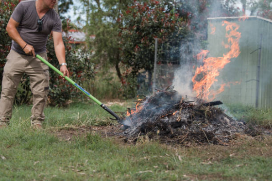 Man burning brush in a backyard. He is holding a poker as he tends the fire.