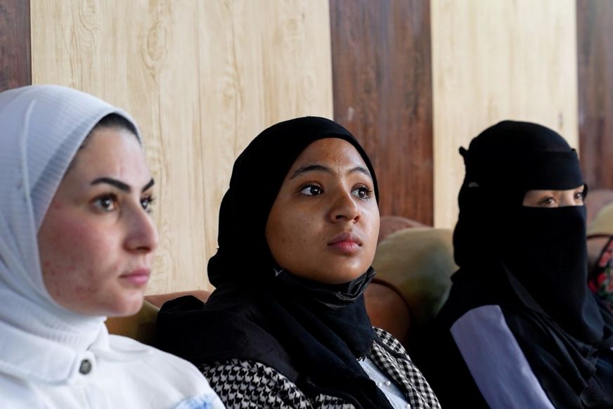 Three young women wearing headscarves look attentively to the right.