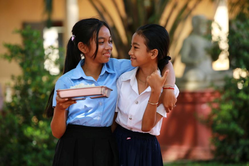 Chandy, holding a meal tray, laughs with a friend outside their school.