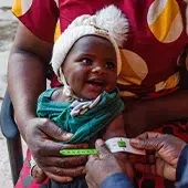 A world vision staff is measuring a baby’s arm during a health check.