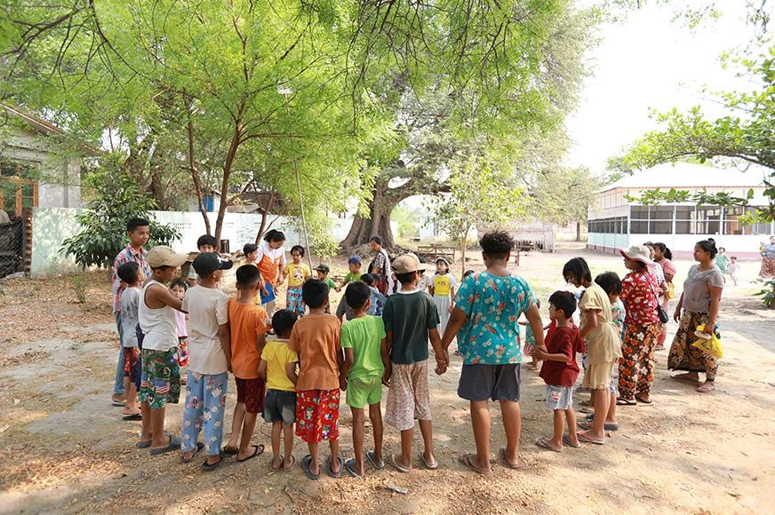 A group of children stand together and hold hands outdoors in Myanmar.