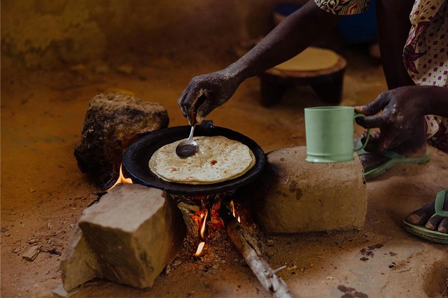 A woman prepares a flatbread over a fire and make-shift stove.