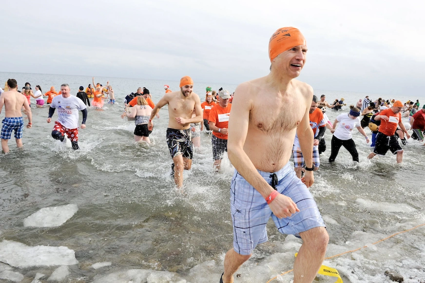 A large group of people run into and out of a cold lake, wearing orange World Vision swim caps.