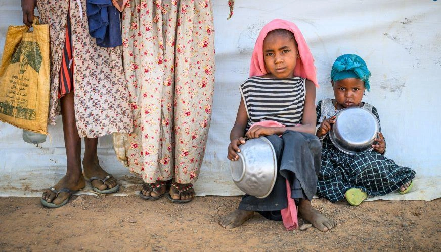 Two Sudanese refugee children wait with empty bowls at a feeding program.