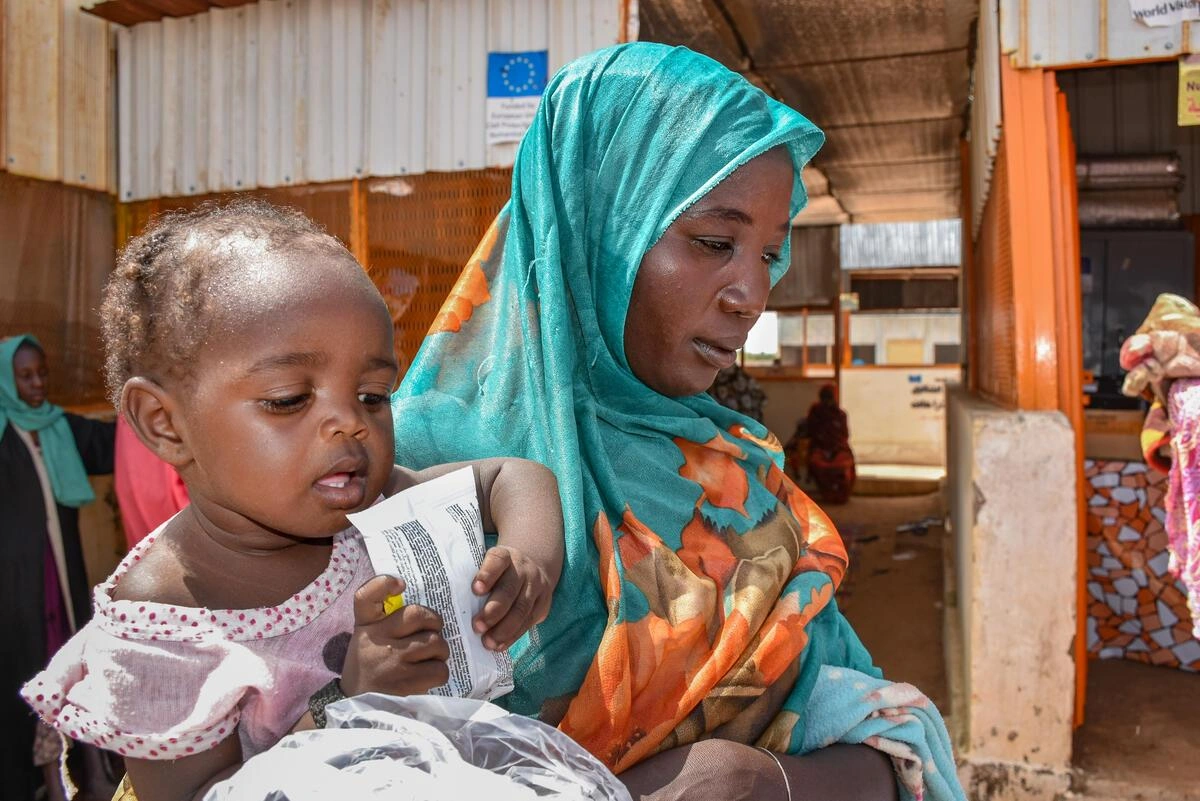 A mother holds a child who is eating supplementary food from an envelope.