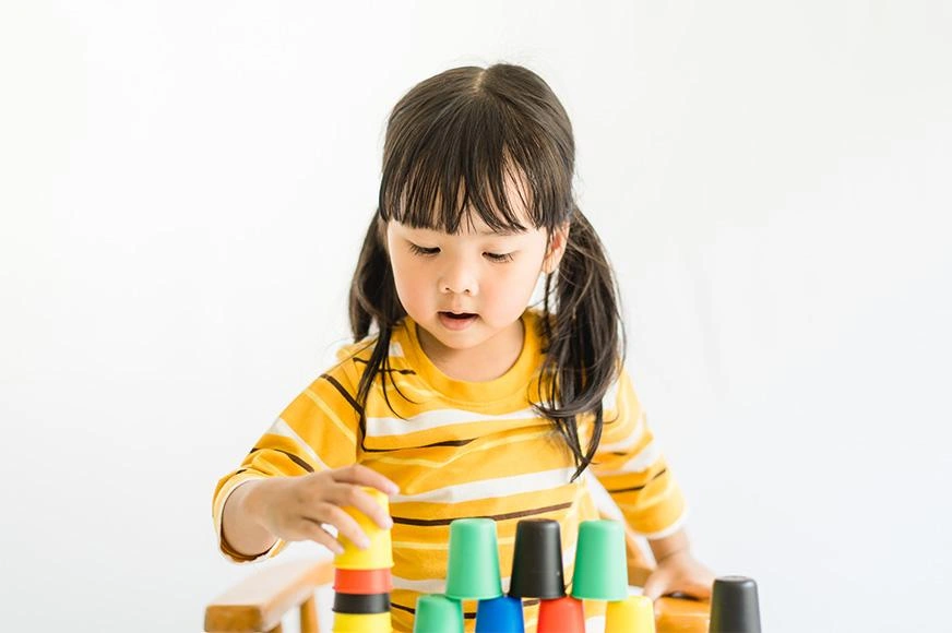 A toddler stacks multi-coloured cups.