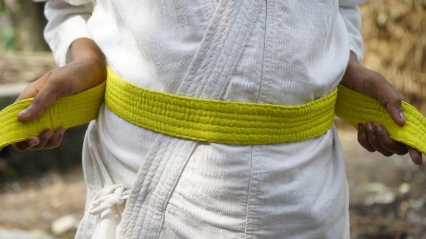 Closeup of a child’s waist, as they tighten their yellow karate belt with their hands.