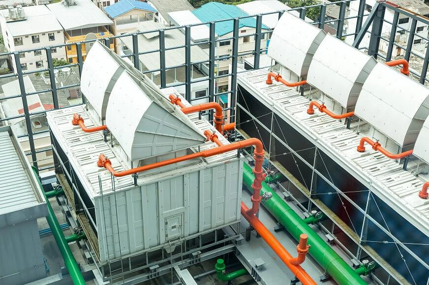 Rooftop industrial cooling units with orange and green piping, used for temperature control in a densely populated city area.