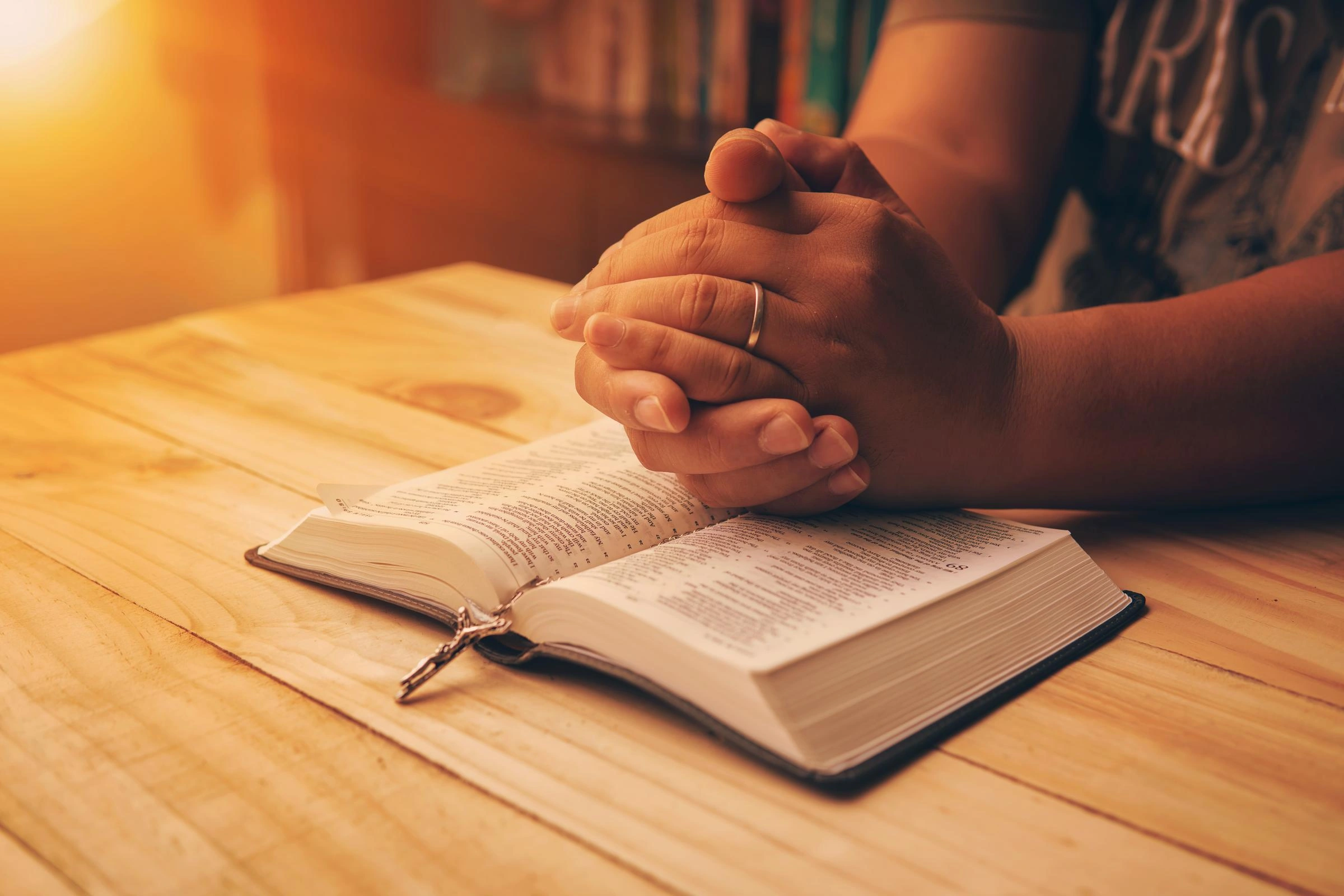 A person sits with folded hands on top of their Bible, symbolizing prayer and devotion.