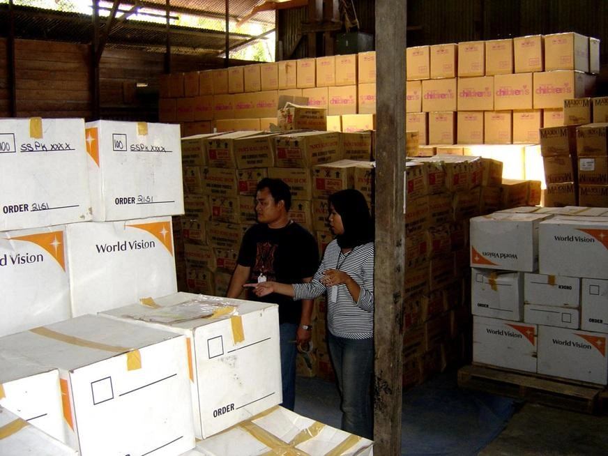 A man and a woman are in a warehouse, taking inventory of World Vision relief goods (Indonesia, 2005)