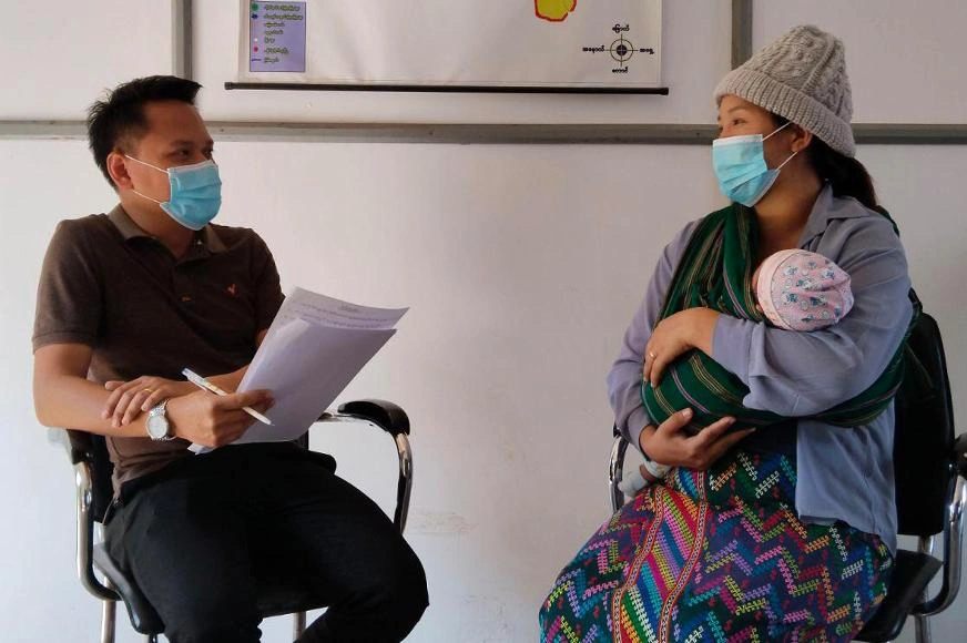 Mai cradles her son, Gam, as she consults with a health worker at the Lashio Health Commission clinic.