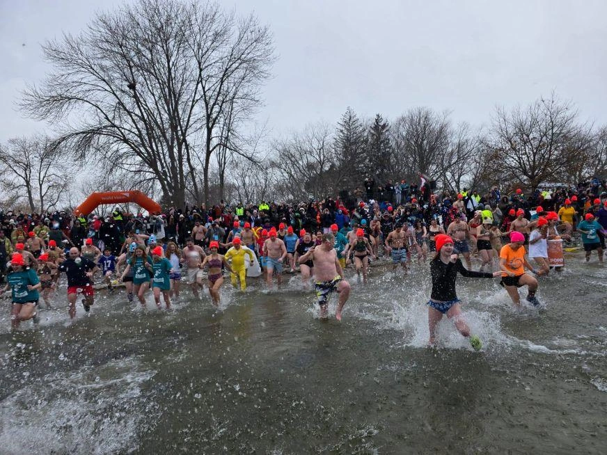 A large group of people wearing bright orange hats run into Lake Ontario.