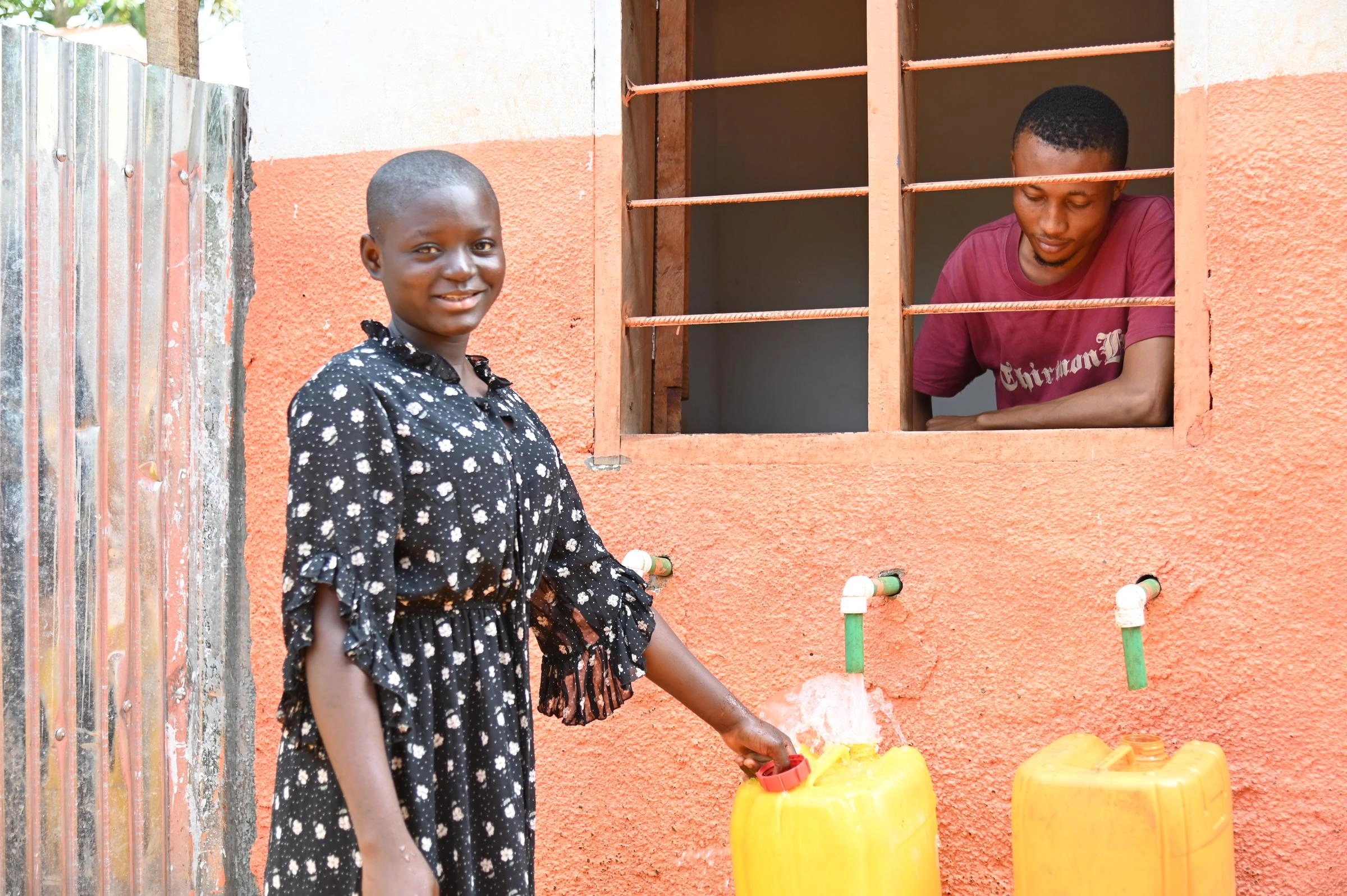 A young girl stands beside a tap, filling a yellow bucket with water.