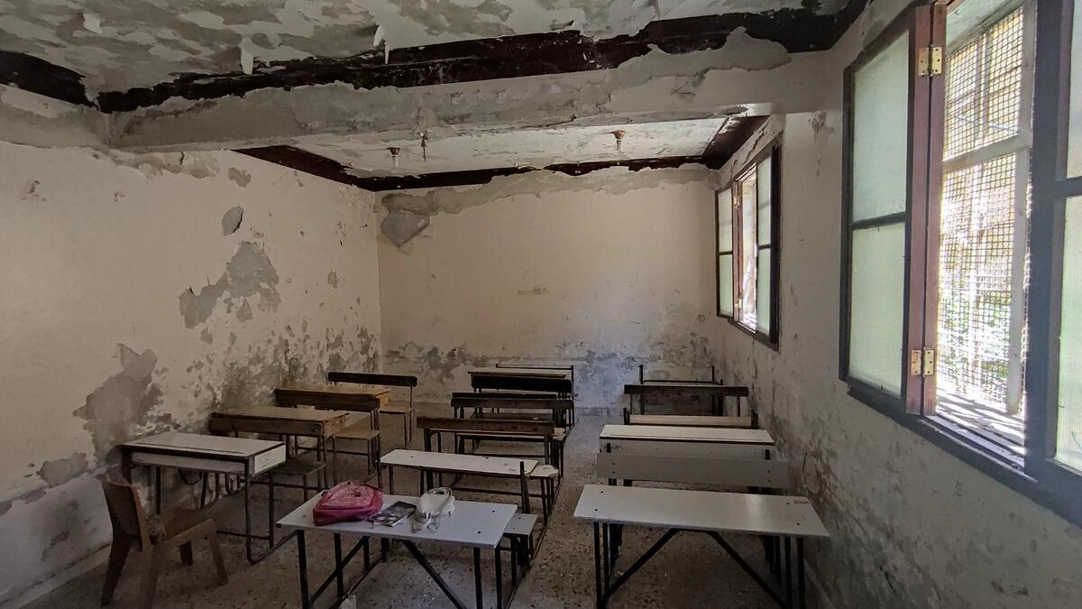 Rows of empty desks sit in an old, dilapidated classroom (Syria, 2022)