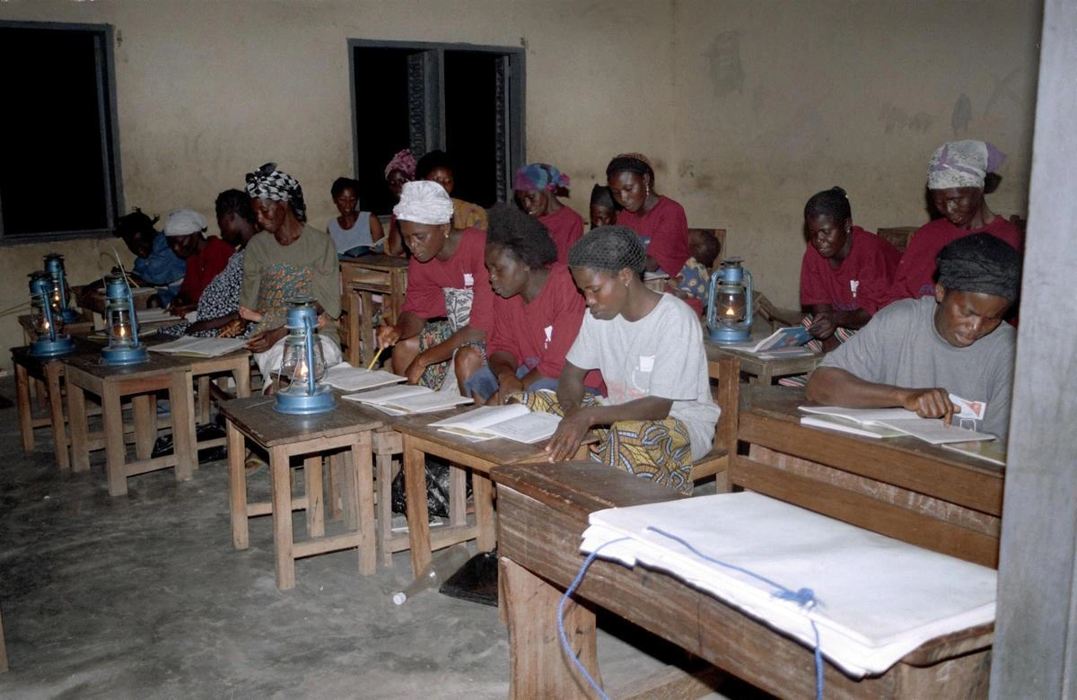 Group of women seated at wooden desks studying in a classroom setting with lamplight.
