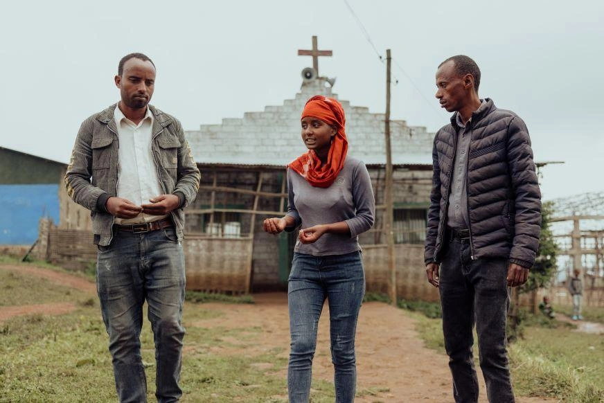 In Ethiopia, a teenage girl walks with two men, speaking and gesturing.
