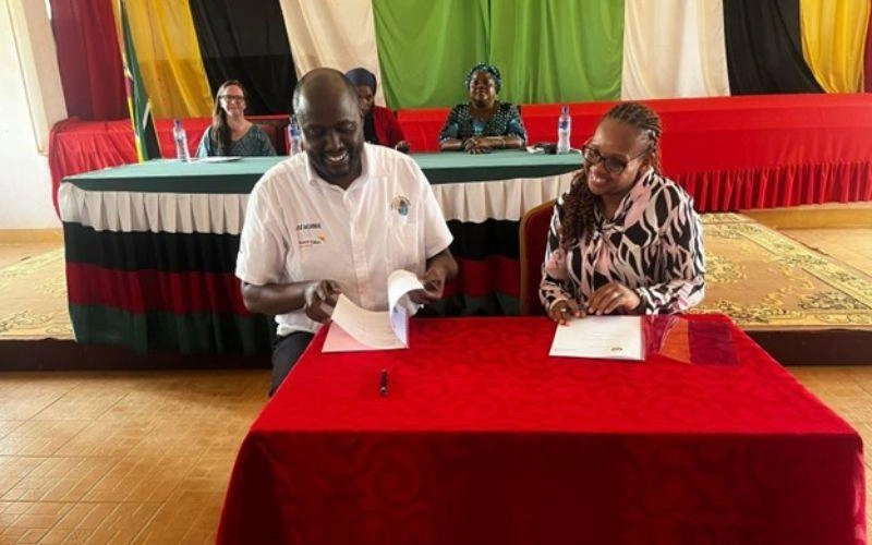 A man and a woman sit at a desk and sign a document together.