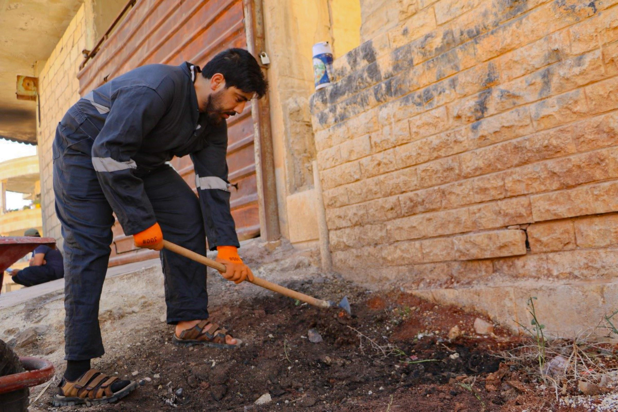 A man in wearing coveralls digs outdoors, as part of a cash-for-work program offered by World Vision.
