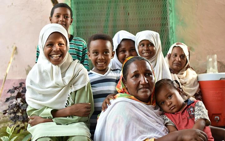 A woman sits, surrounded by children, cuddling a young child in her lap.
