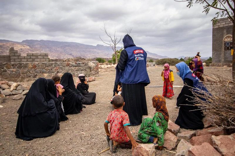 Yemeni women and children sitting on the ground outdoors.