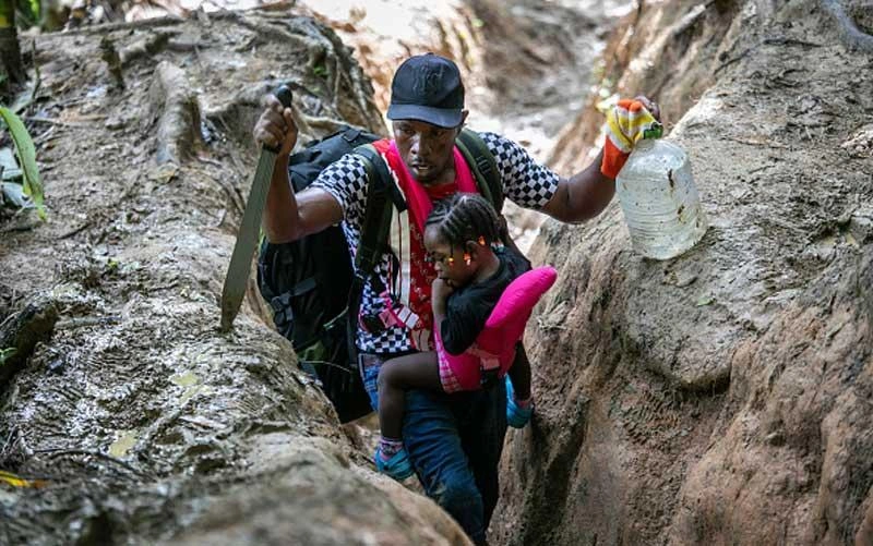 darien-gap-migrant-route-man-carrying-child-walking-through-a-ditch