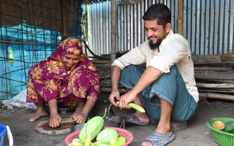 Muslima and Abu sit together in their home, preparing vegetables for cooking.