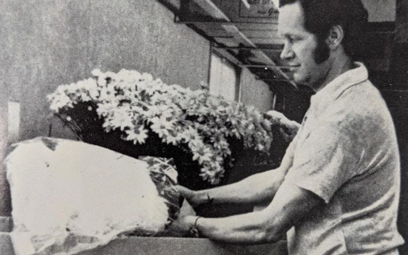 Black-and-white image of a man packaging flowers for delivery.