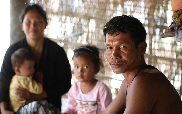 A man faces toward the camera. Behind him are a woman and two young children.