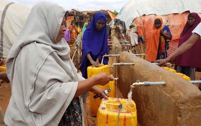 In Somalia, several women gather around borehole taps to fill yellow buckets with water.