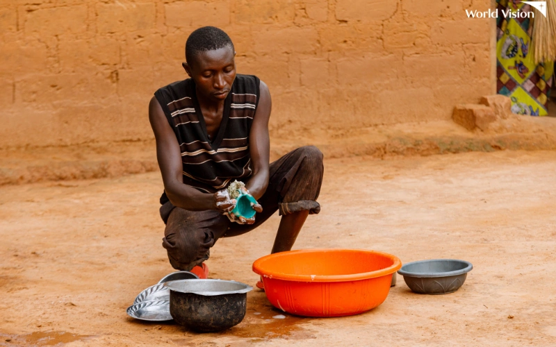 A man is squatting on the floor while washing dishes.