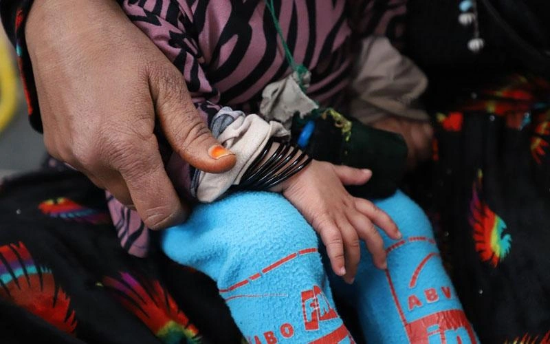 A tiny child sits on the lap of a woman (neither face is visible).