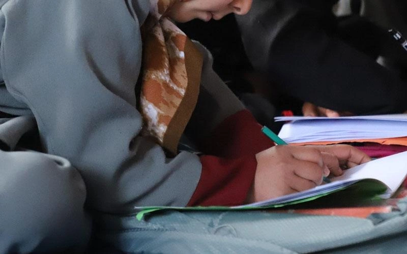 A kindergarten-aged girl writes in a notebook. Photo is cropped to show lower face only.