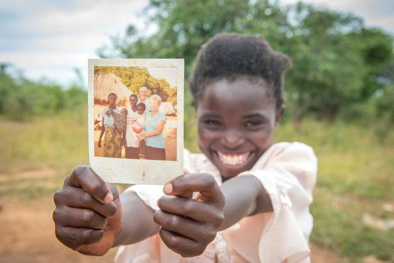 A sponsored girl shows off a picture of her sponsors during their visit to her home in Zambia.