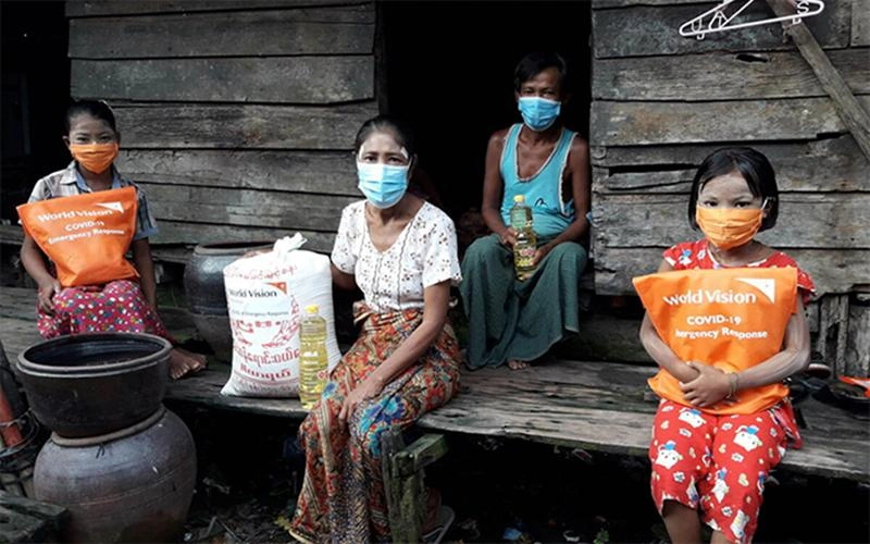 Thandar from Myanmar sits in front of her house with her family and their supply of nutritious ingredients from World Vision.