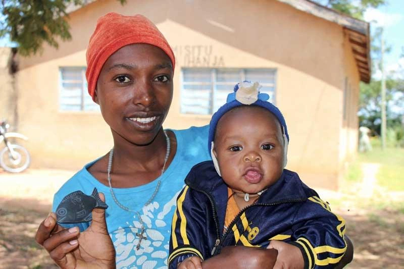 A woman in Tanzania holding her baby and showing off an iron fish.