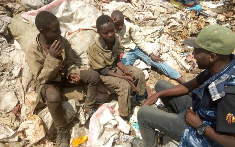 A group of four young men sit on a pile of garbage.