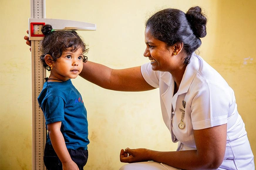 A medical professional measures a young girl's weight on a scale.