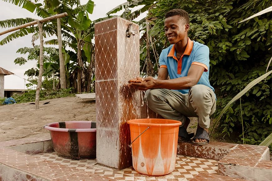 A teenage boy collects water from a community borehole tap. 