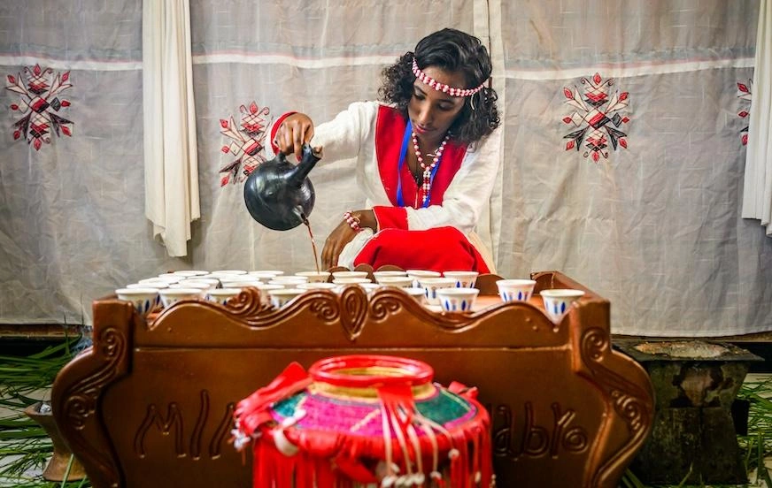 Une femme vêtue d'un costume traditionnel éthiopien verse du café dans des tasses.