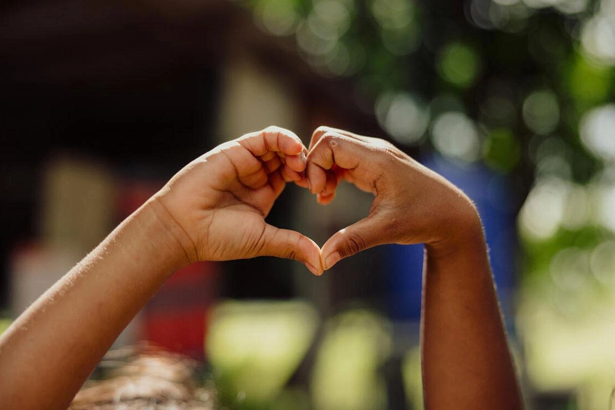 A child's hands making a heart symbol to convey love outside.