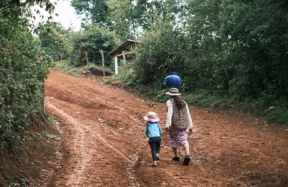 A woman carrying a jug of water on her head walks on a dirt road alongside a young girl. (Honduras, 2023)