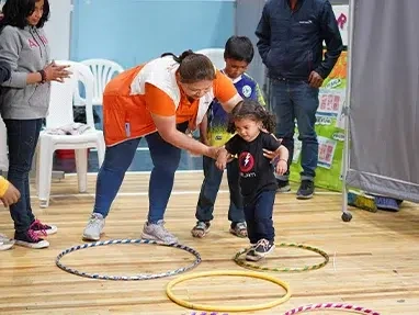 World Vision staff helps a small child jump through hula-hoops at a child friendly space.