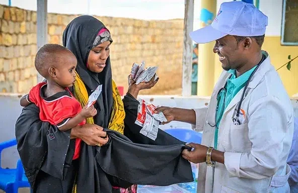 World Vision staff gives mother holding her child packages of ready-to-use therapeutic food at a nutrition center. (Somalia, 2023)