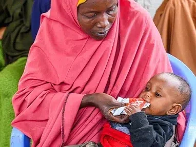 A mother feeds her child Ready-to-Eat Therapeutic nutritional supplement, at the Darusalam Mother and Child Health Center. (Somalia, 2023)
